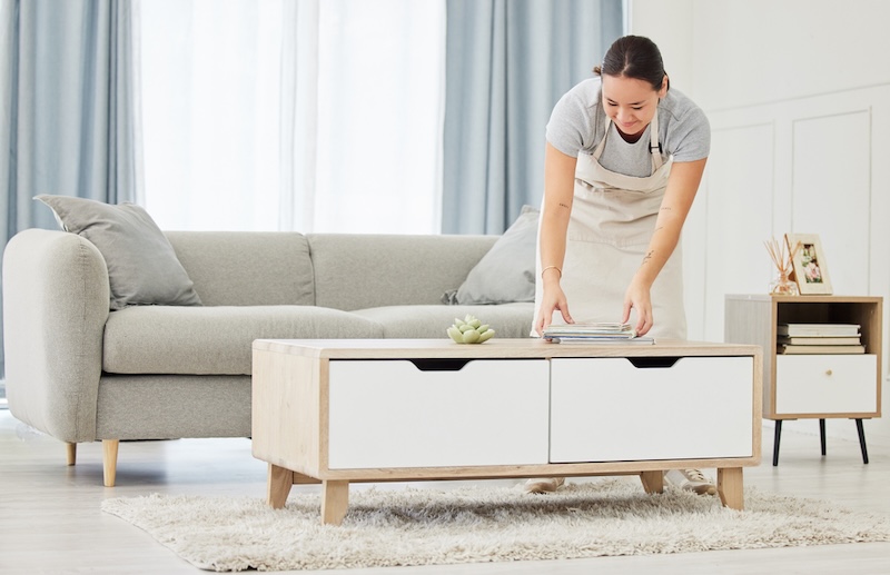 Tricks für ein ordentliches Zuhause - Frau räumt im Wohnzimmer auf